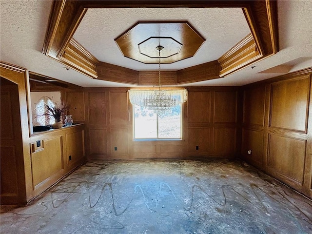 unfurnished dining area with a tray ceiling, wooden walls, a textured ceiling, and a notable chandelier