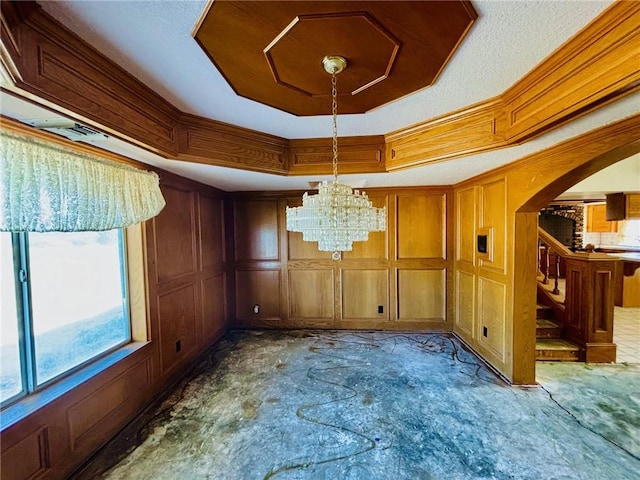 spare room with a tray ceiling, wooden walls, and a notable chandelier