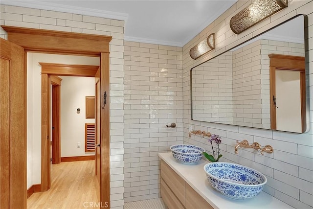 bathroom with ornamental molding, tile walls, sink, and wood-type flooring