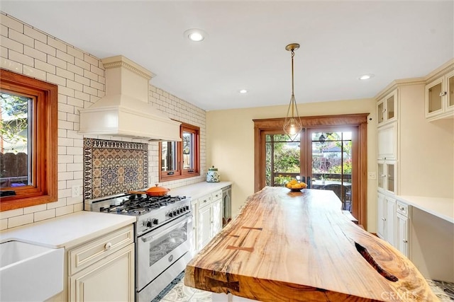 kitchen featuring custom exhaust hood, hanging light fixtures, butcher block countertops, backsplash, and high end stainless steel range