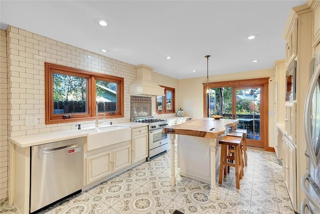 kitchen with stainless steel appliances, hanging light fixtures, premium range hood, a kitchen island, and butcher block counters