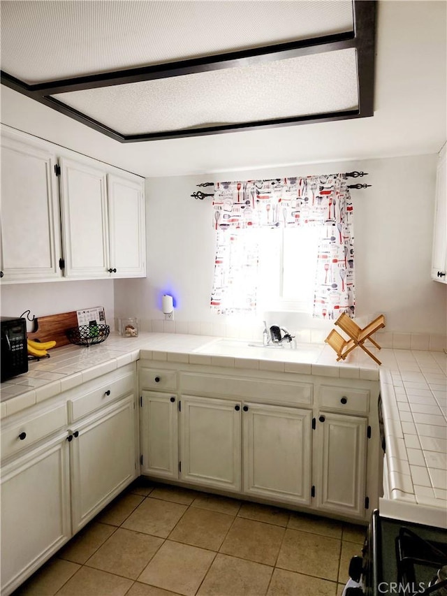 kitchen with tile countertops, sink, light tile patterned floors, and stove