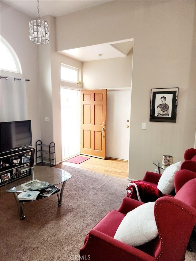 living room with a chandelier, a towering ceiling, a healthy amount of sunlight, and carpet flooring