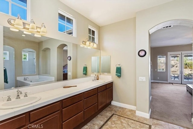 full bathroom featuring double vanity, a bath, baseboards, and a sink