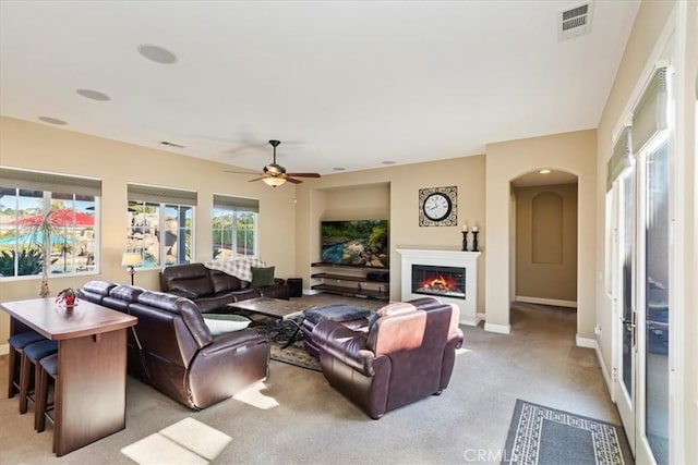 living room with visible vents, baseboards, light colored carpet, arched walkways, and a ceiling fan