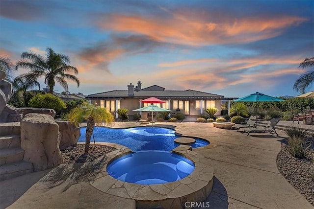 pool at dusk featuring a patio area and an in ground hot tub