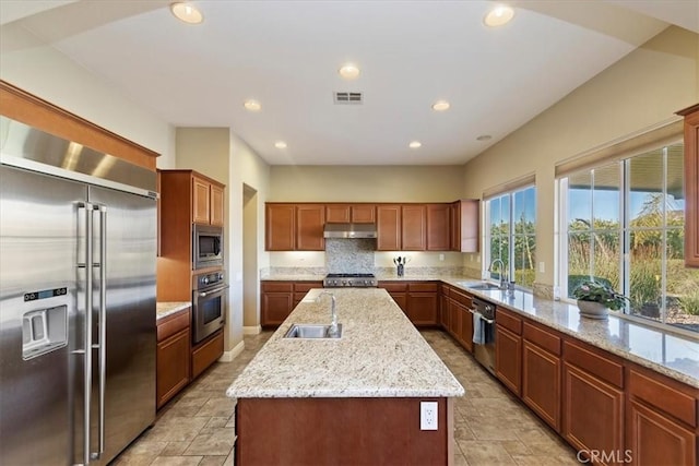 kitchen with a sink, built in appliances, under cabinet range hood, and an island with sink