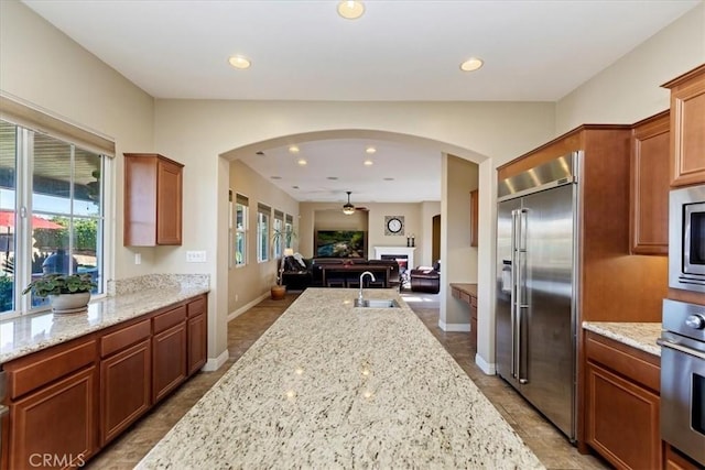 kitchen featuring built in appliances, recessed lighting, a sink, open floor plan, and light stone countertops