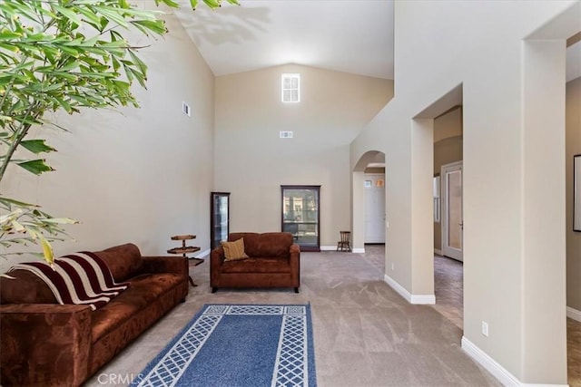 carpeted living room with arched walkways, high vaulted ceiling, visible vents, and baseboards