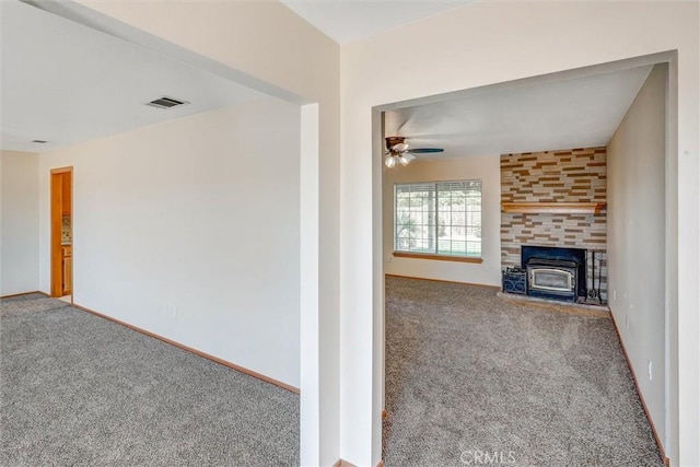 unfurnished living room with a wood stove, ceiling fan, and carpet