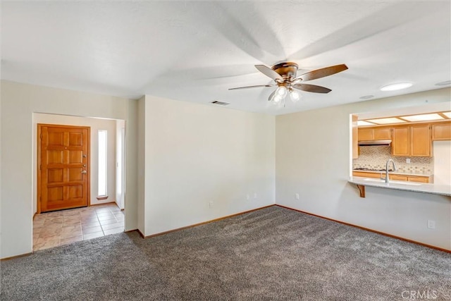 unfurnished living room featuring ceiling fan, light colored carpet, and sink