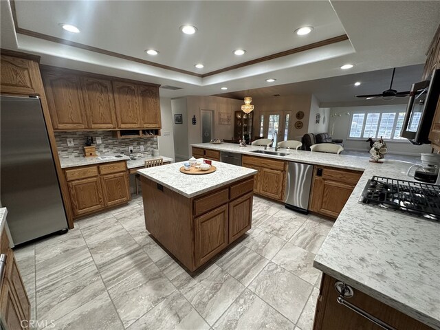 kitchen with a raised ceiling, sink, appliances with stainless steel finishes, a kitchen island, and kitchen peninsula