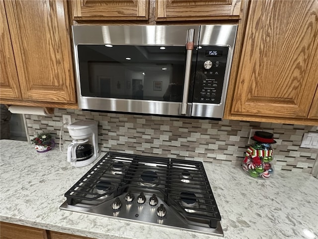 kitchen with stainless steel appliances, light stone countertops, and backsplash