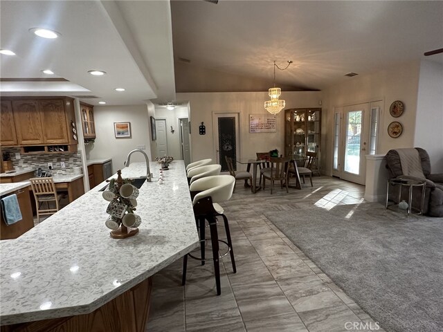 kitchen with a kitchen bar, light colored carpet, sink, decorative light fixtures, and light stone counters