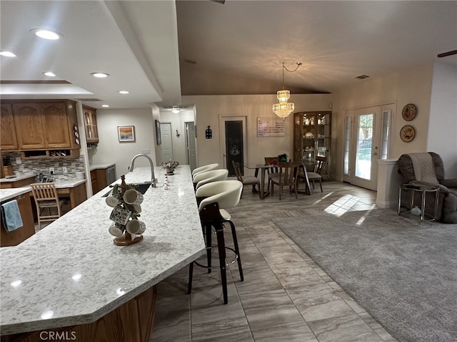 kitchen with a kitchen bar, sink, light stone counters, tasteful backsplash, and pendant lighting