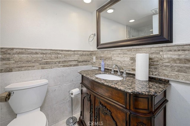 bathroom featuring toilet, vanity, and tile walls