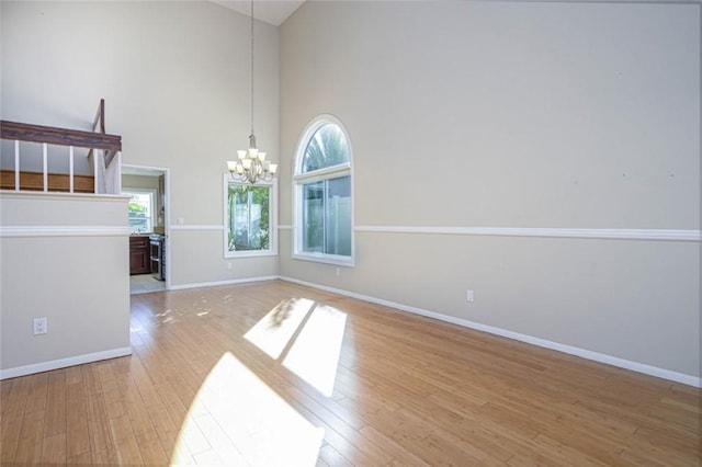 empty room featuring light hardwood / wood-style flooring, an inviting chandelier, and high vaulted ceiling