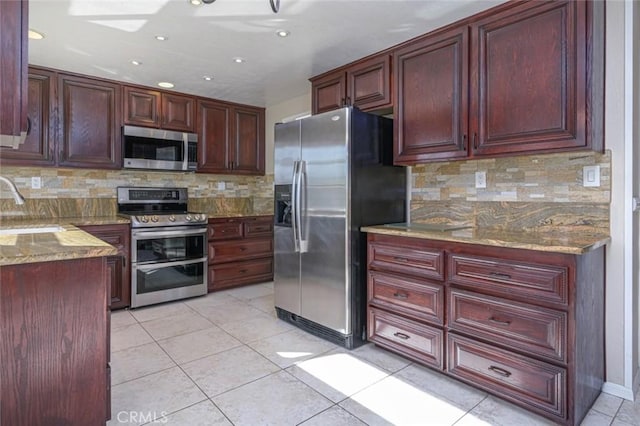 kitchen with sink, light stone counters, tasteful backsplash, light tile patterned floors, and appliances with stainless steel finishes