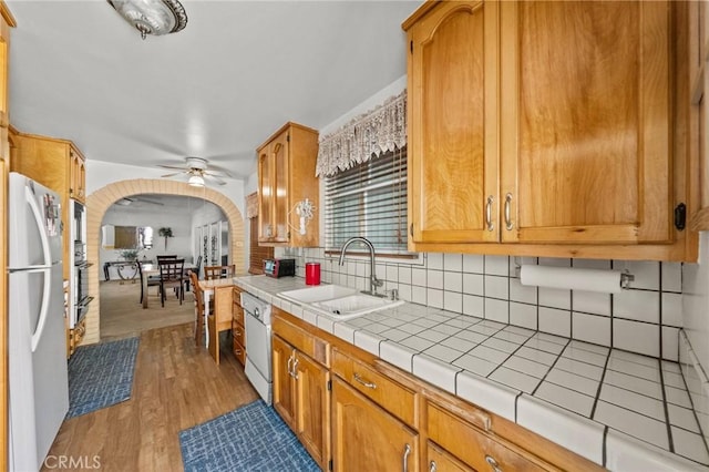 kitchen with ceiling fan, tile countertops, sink, light hardwood / wood-style flooring, and stainless steel fridge