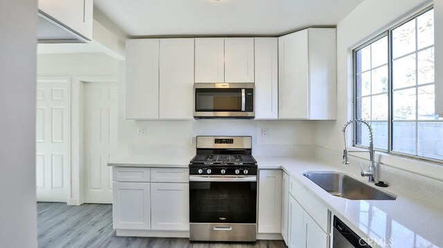 kitchen featuring light stone counters, light hardwood / wood-style floors, white cabinetry, appliances with stainless steel finishes, and sink