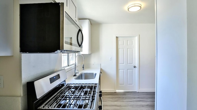 kitchen with sink, stainless steel appliances, white cabinetry, and light hardwood / wood-style flooring