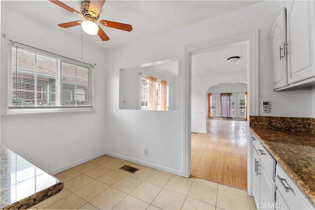 kitchen with light tile patterned floors, ceiling fan, dark stone counters, a wealth of natural light, and white cabinets