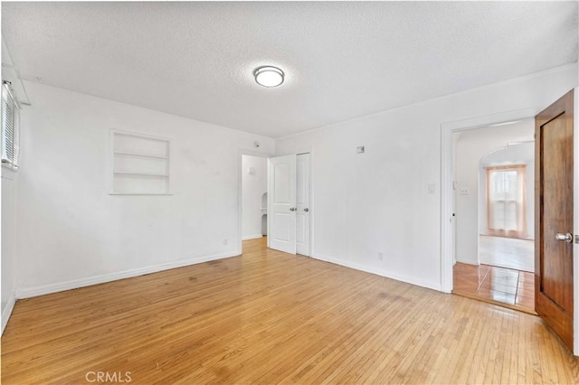 spare room featuring light wood-type flooring, built in features, and a textured ceiling