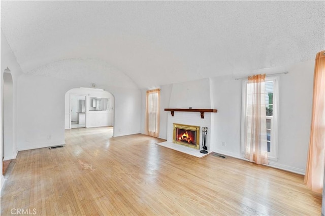 unfurnished living room with a textured ceiling, lofted ceiling, and light hardwood / wood-style floors