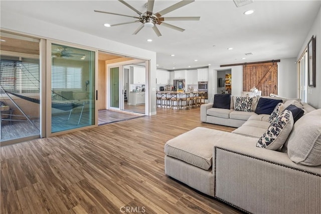 living room with ceiling fan, a barn door, and wood-type flooring