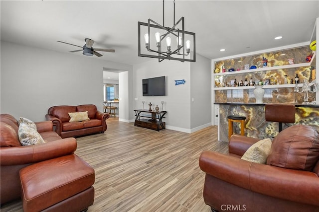 living room with ceiling fan with notable chandelier, built in shelves, and light hardwood / wood-style flooring