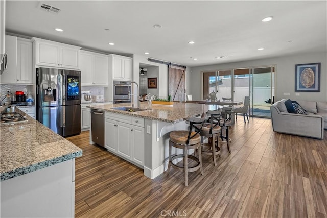 kitchen featuring a center island with sink, sink, a barn door, white cabinetry, and stainless steel appliances