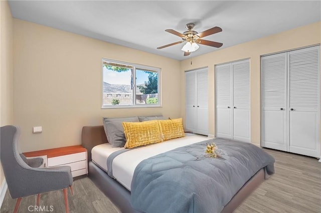 bedroom featuring hardwood / wood-style floors, multiple closets, and ceiling fan