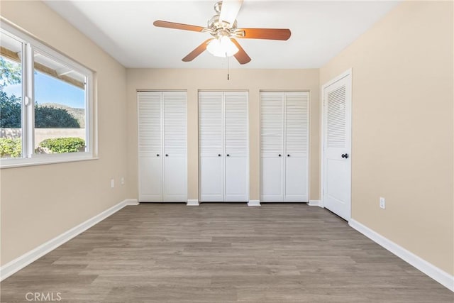 unfurnished bedroom featuring light wood-type flooring, ceiling fan, and multiple closets