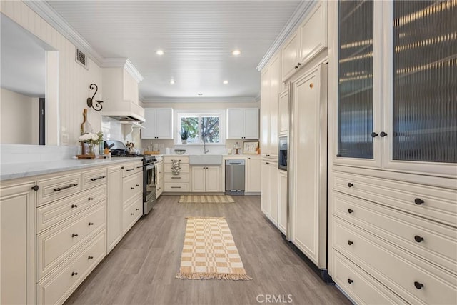 kitchen with white cabinetry, light stone counters, light wood-type flooring, crown molding, and appliances with stainless steel finishes