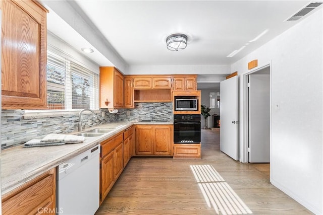 kitchen with stainless steel microwave, sink, tasteful backsplash, white dishwasher, and oven