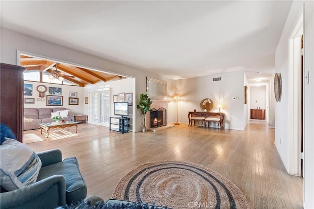 living room with ceiling fan, wooden ceiling, a brick fireplace, vaulted ceiling with beams, and light hardwood / wood-style floors