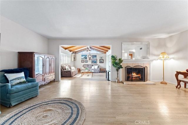 living area with a fireplace, light wood-type flooring, vaulted ceiling with beams, and ceiling fan