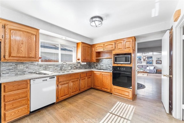 kitchen featuring light wood-type flooring, tasteful backsplash, sink, dishwasher, and black oven