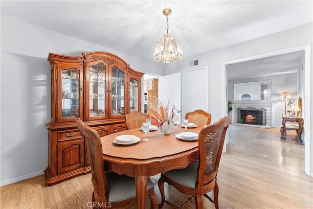 dining room featuring a chandelier, light hardwood / wood-style floors, and a brick fireplace