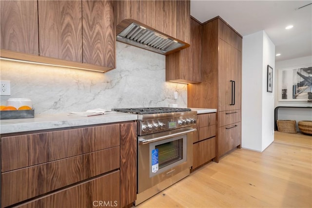 kitchen with high end range, backsplash, premium range hood, and light hardwood / wood-style floors