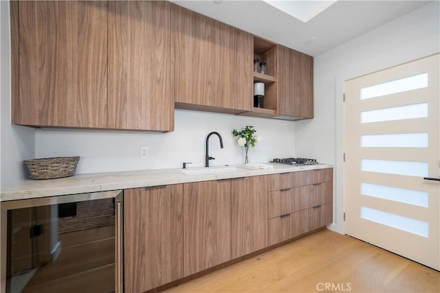 kitchen featuring stainless steel gas stovetop, light hardwood / wood-style floors, sink, and beverage cooler