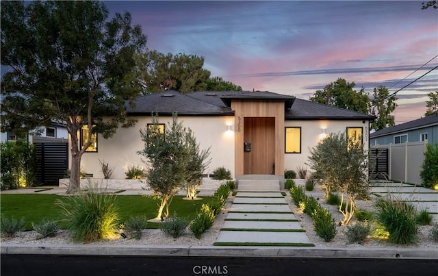 view of front facade featuring stucco siding, a yard, and fence