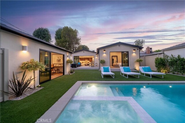 back house at dusk featuring a lawn