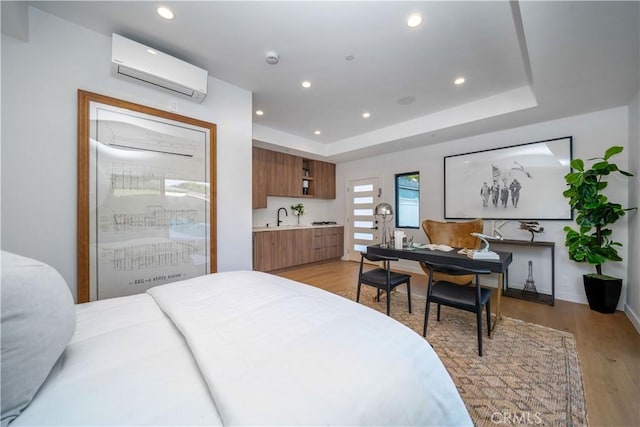 bedroom featuring an AC wall unit, sink, a tray ceiling, and light hardwood / wood-style floors