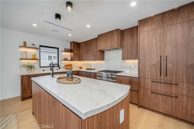 kitchen with backsplash, an island with sink, stainless steel range, and light hardwood / wood-style flooring