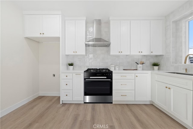 kitchen featuring gas stove, white cabinetry, sink, and wall chimney range hood