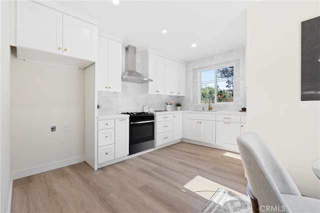 kitchen with sink, light hardwood / wood-style flooring, wall chimney exhaust hood, range with gas stovetop, and white cabinetry