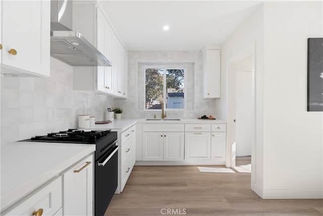 kitchen featuring backsplash, black gas range oven, sink, wall chimney range hood, and white cabinetry