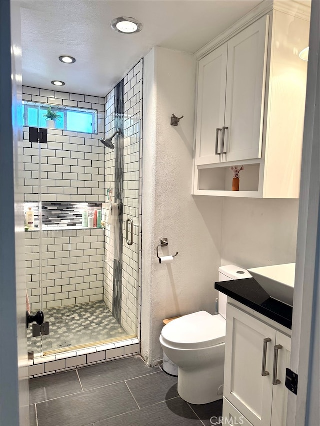 bathroom featuring toilet, vanity, tile patterned flooring, and a shower with shower door