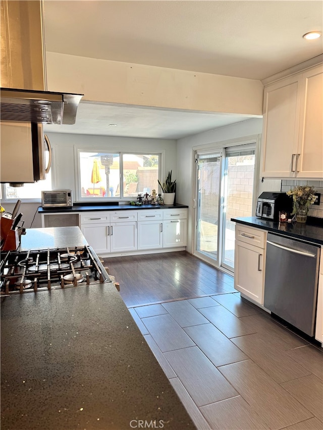 kitchen with white cabinetry, wood-type flooring, backsplash, exhaust hood, and appliances with stainless steel finishes